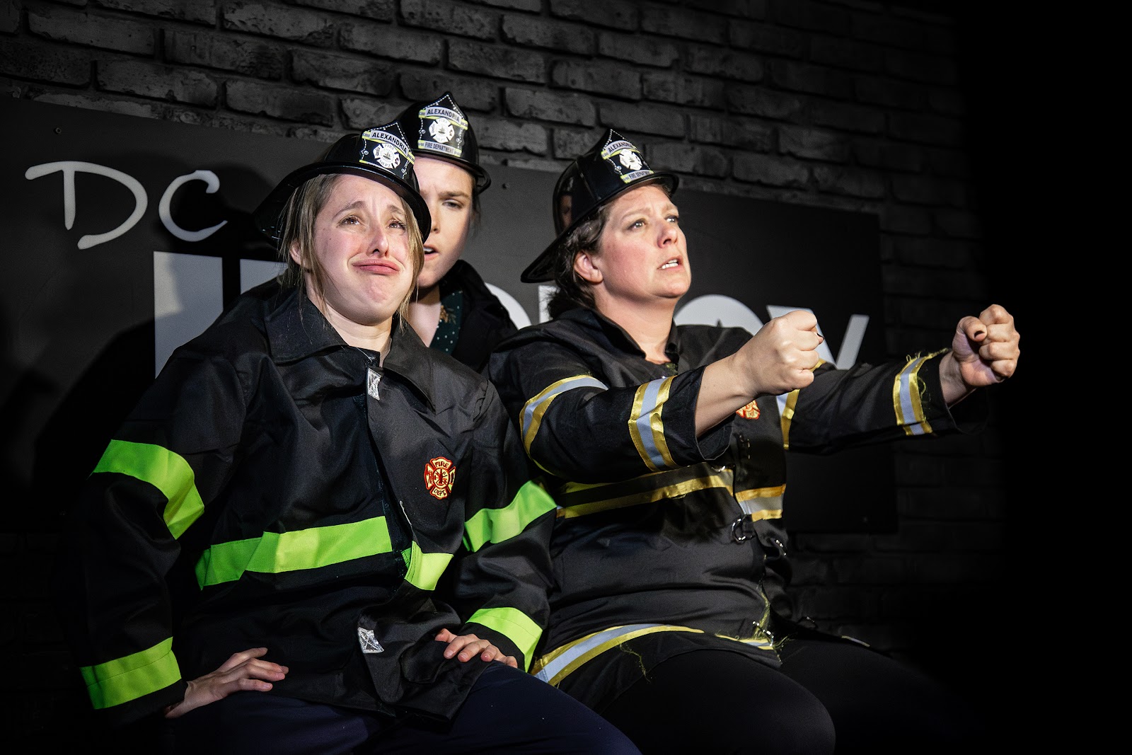 Four performers in firefighter turnout gear striking poses on stage.